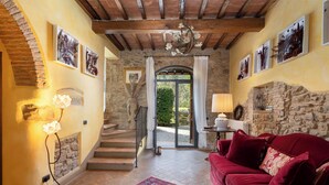 A cozy living room with a red sofa, a patterned rug, and a staircase leading to a door with a view of greenery outside. - L'antica Meletta (Gambassi Terme)