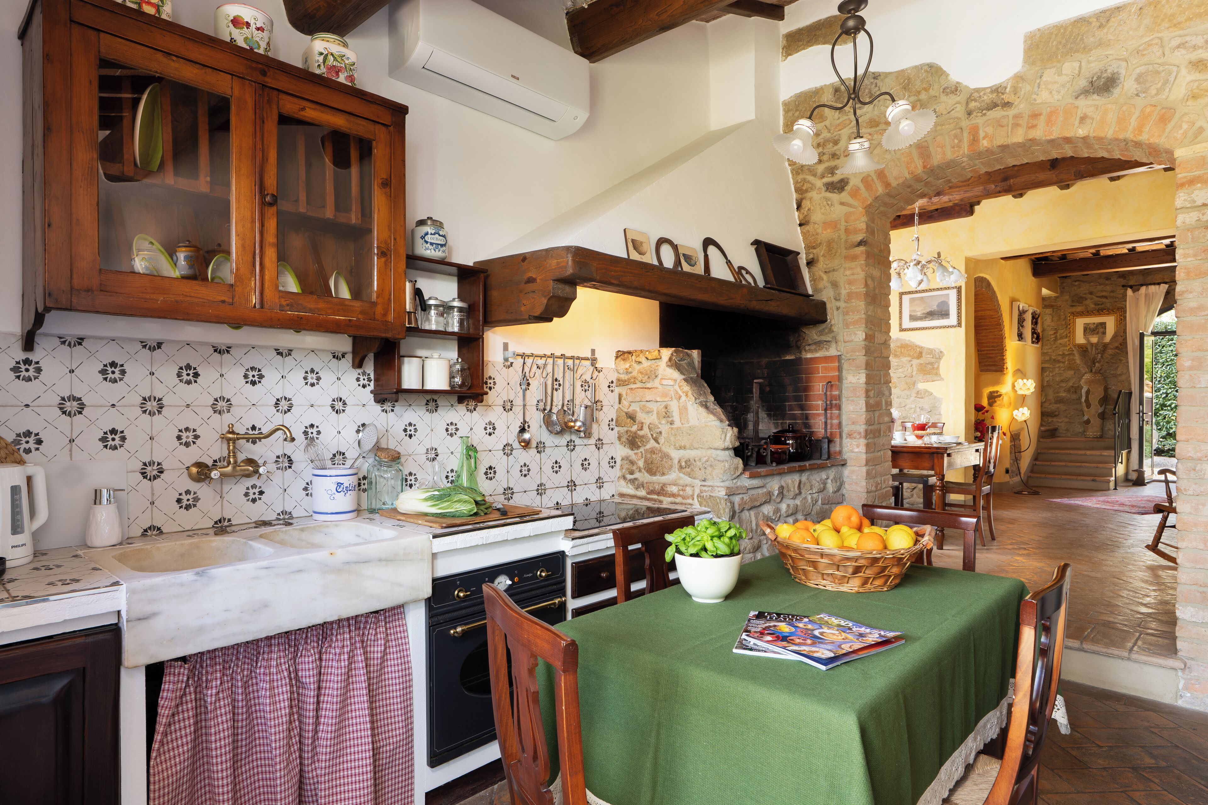 A rustic kitchen with a stone fireplace, wooden cabinets, and a dining area with a green tablecloth.