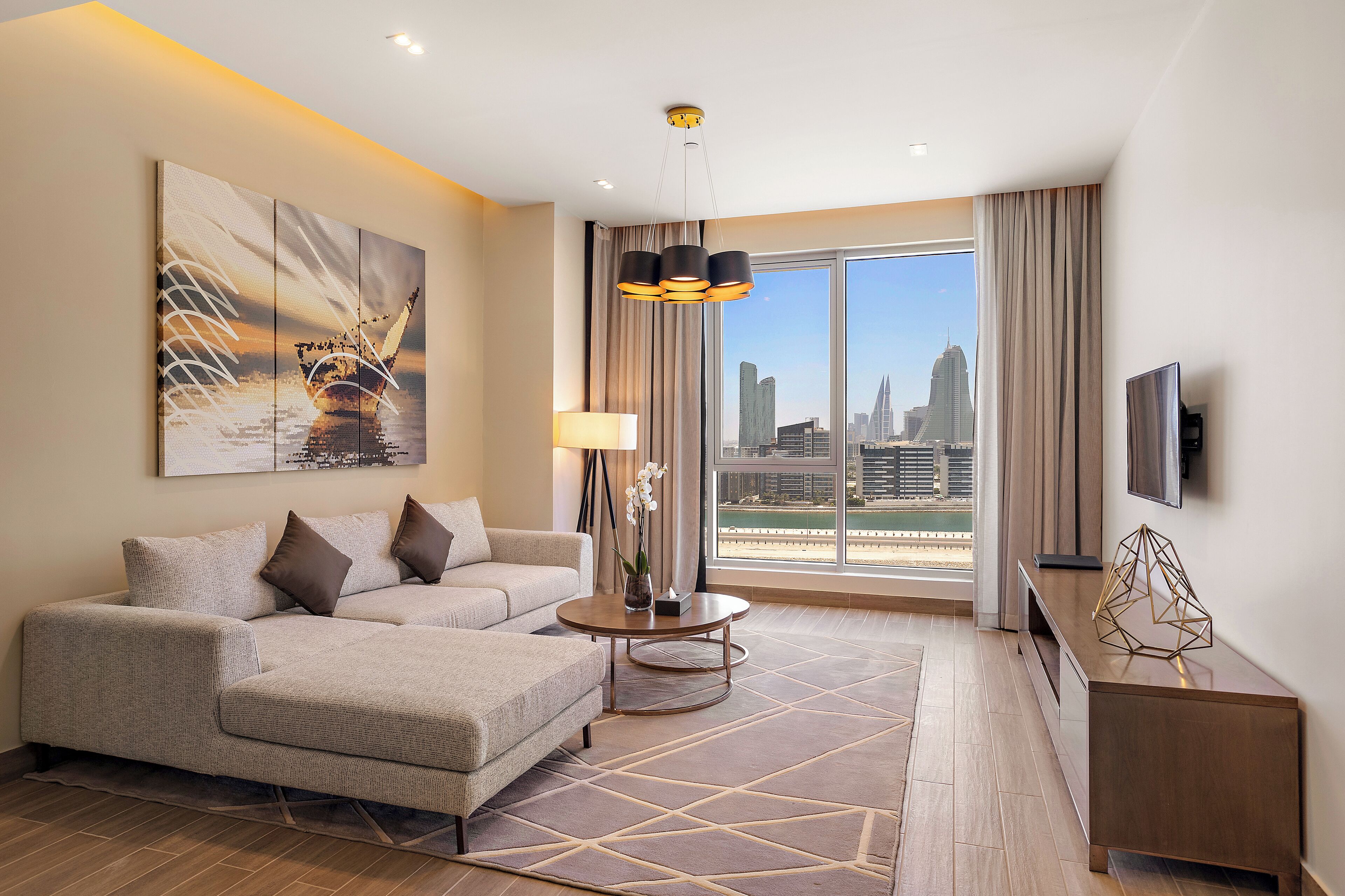 Une chambre d’hôtel moderne dotée d’une grande fenêtre donnant sur la ville, d’un canapé, d’une table basse et d’un téléviseur posé sur un meuble.