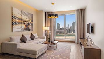 Une chambre d’hôtel moderne dotée d’une grande fenêtre donnant sur la ville, d’un canapé, d’une table basse et d’un téléviseur posé sur un meuble.