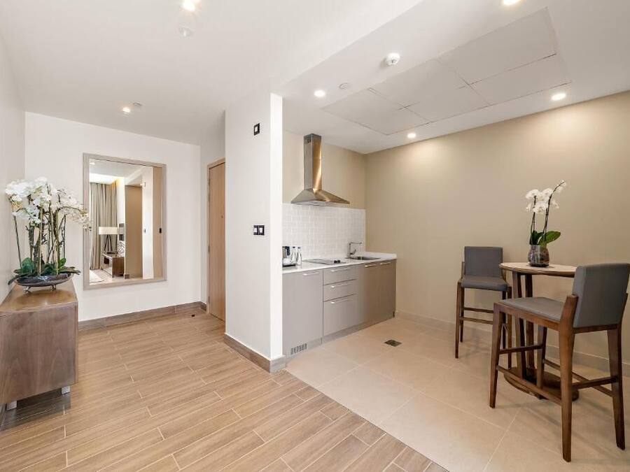 A modern kitchen with white cabinets, a stainless steel range hood, and a dining area with a table and chairs.