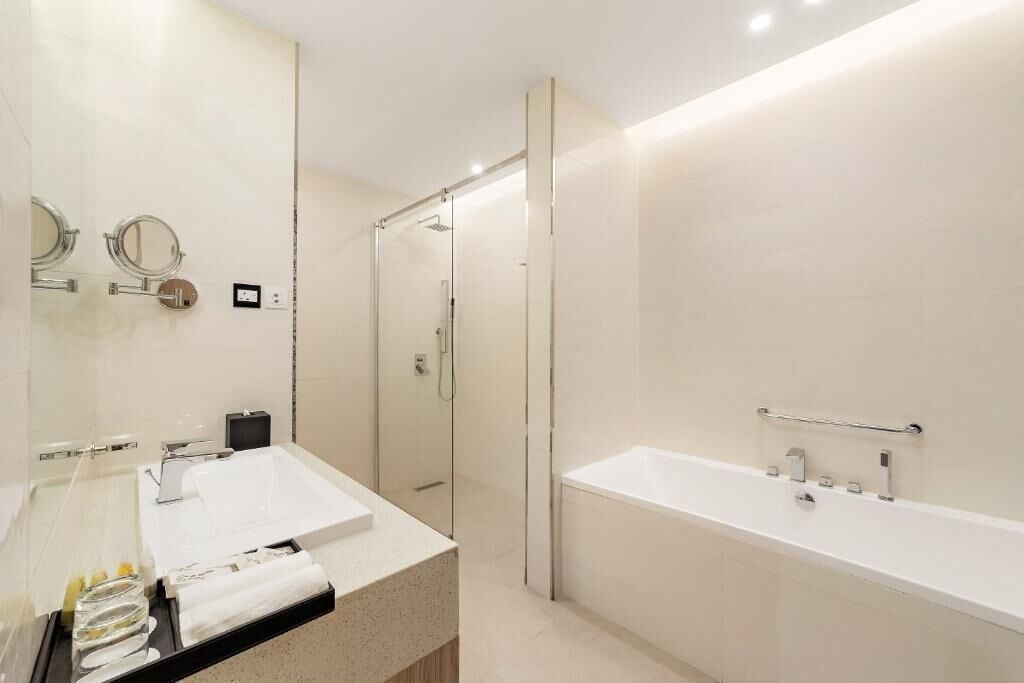 Un baño moderno con ducha envuelta en vidrio, una bañera blanca grande y un lavabo con espejo sobre encimera.