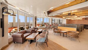 Un espace de détente moderne avec des canapés en cuir, des tables en bois et un bar agrémenté d’un mur en briques et de luminaires suspendus.