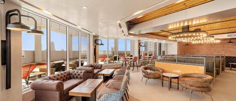 A modern lounge area with leather sofas, wooden tables, and a bar area with a brick wall and hanging lights.