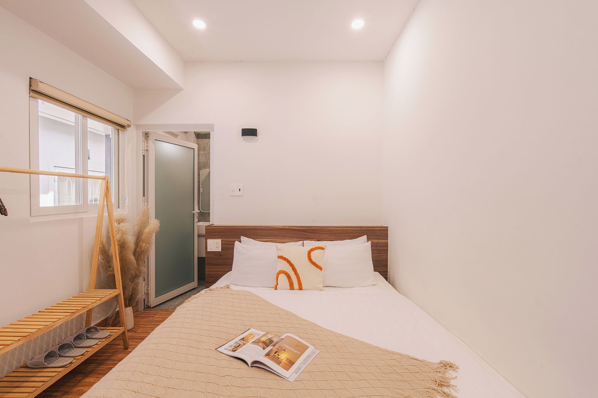 A bedroom with a bed, a wooden shoe rack, a magazine on the bed, and a door leading to another room.