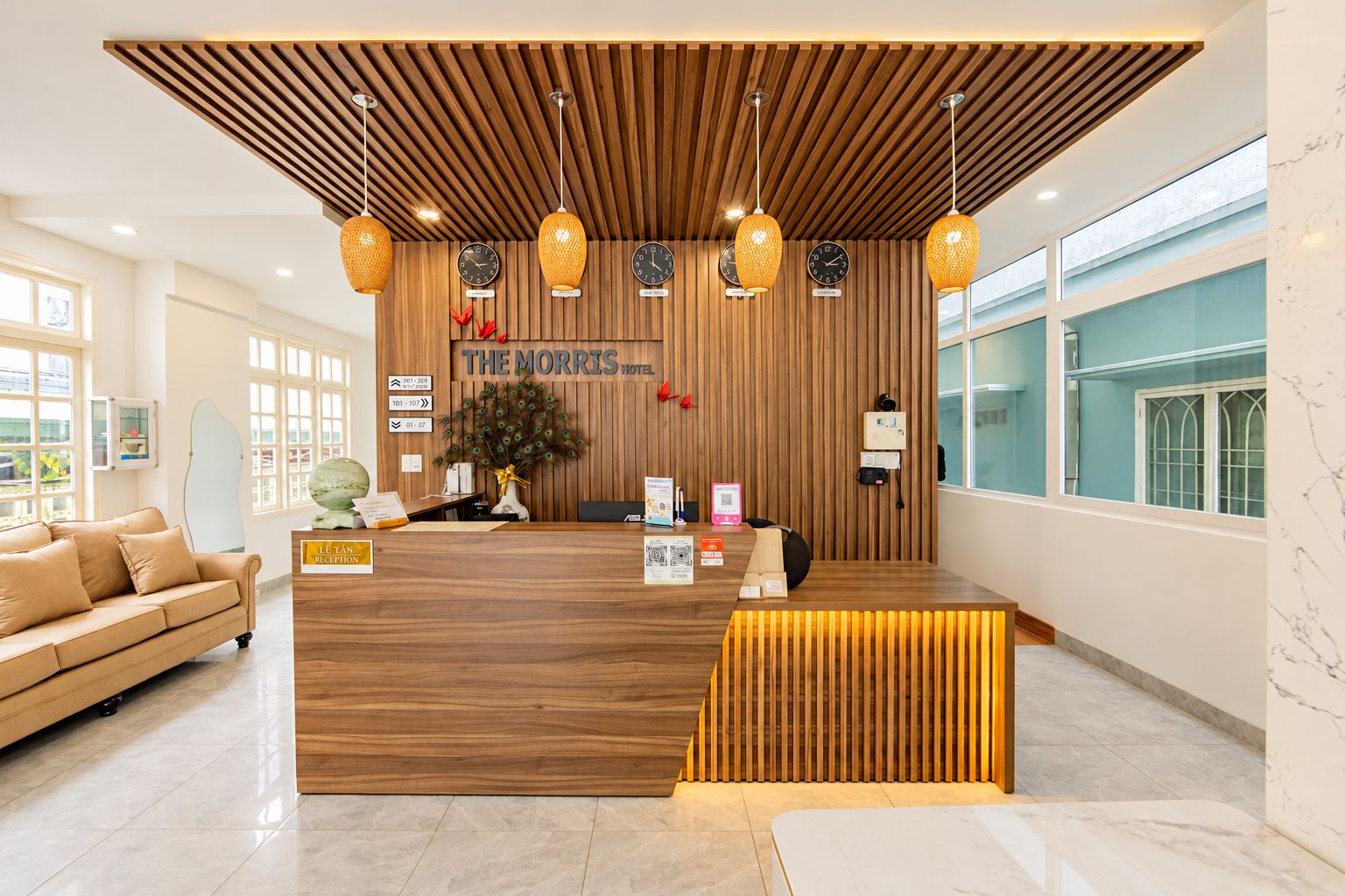 A hotel reception area with a wooden reception desk, multiple clocks, and a peacock decoration.