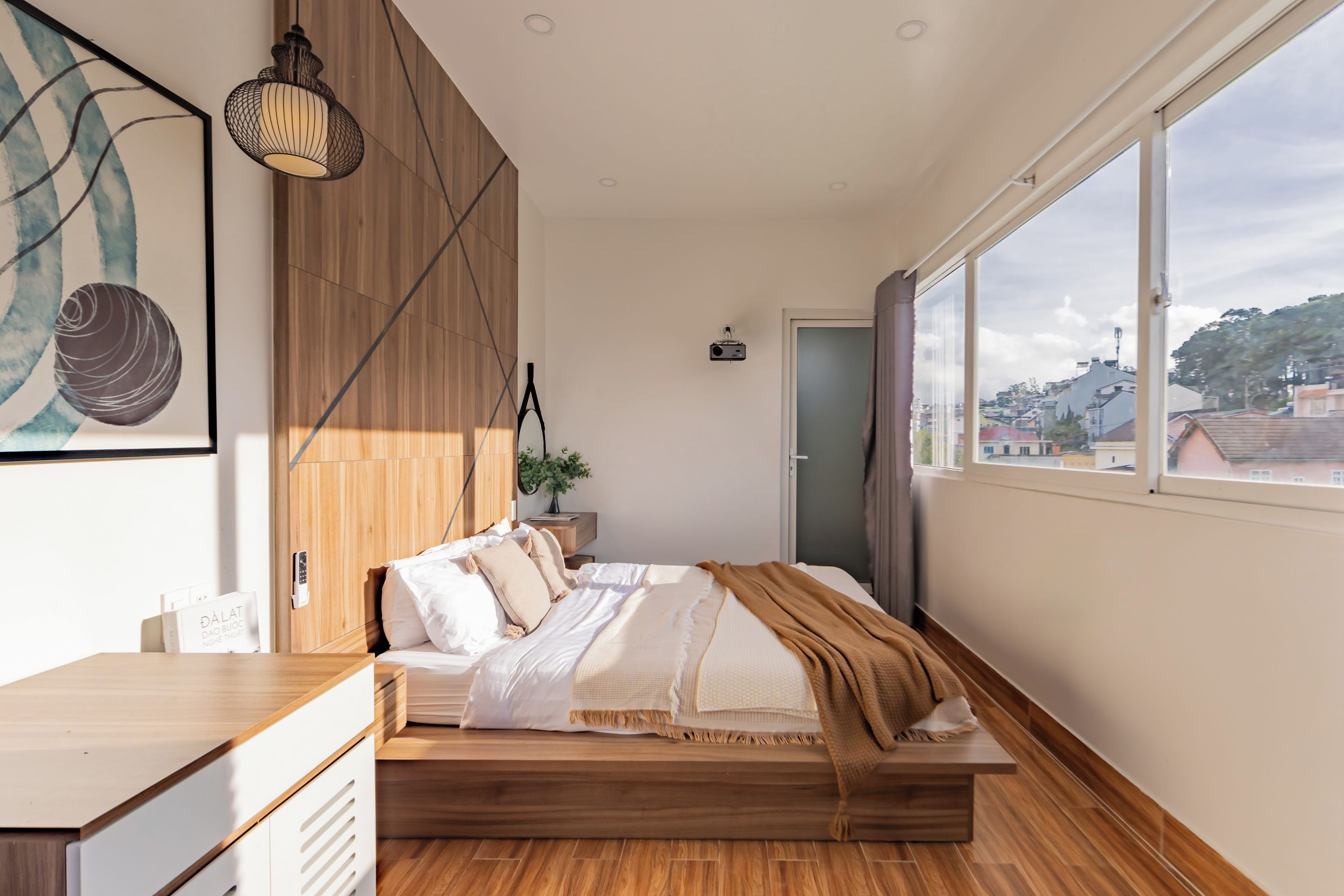 A modern bedroom with a wooden bed, a large window, and a view of the city.
