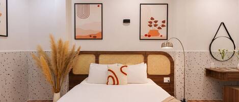 A modern hotel room with a bed, a nightstand, a lamp, and abstract wall art.