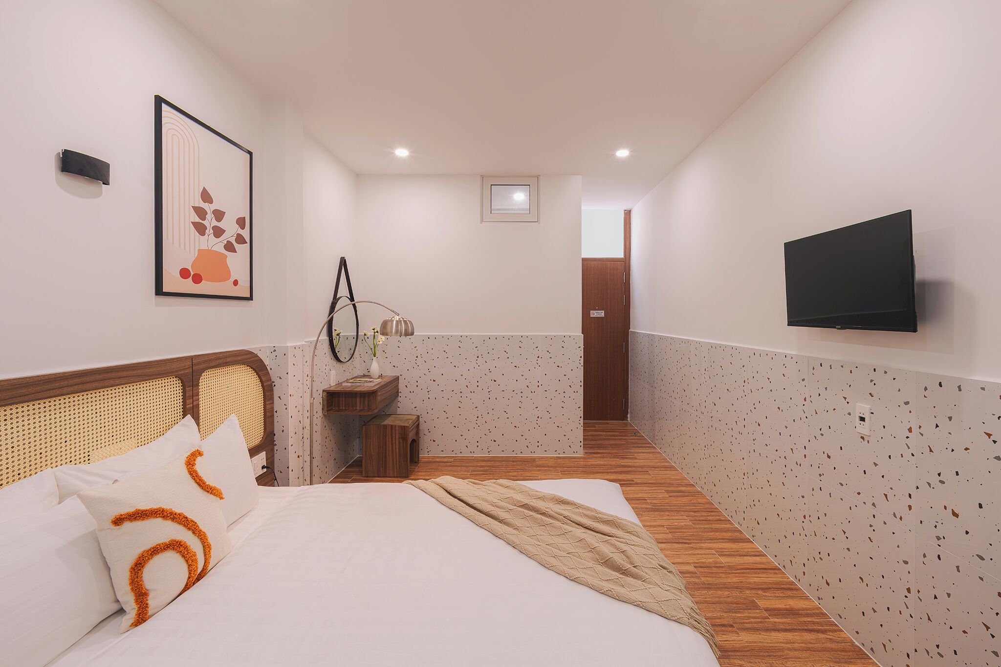 A hotel room with a bed, a flat-screen TV, a framed artwork, and a small wooden side table.
