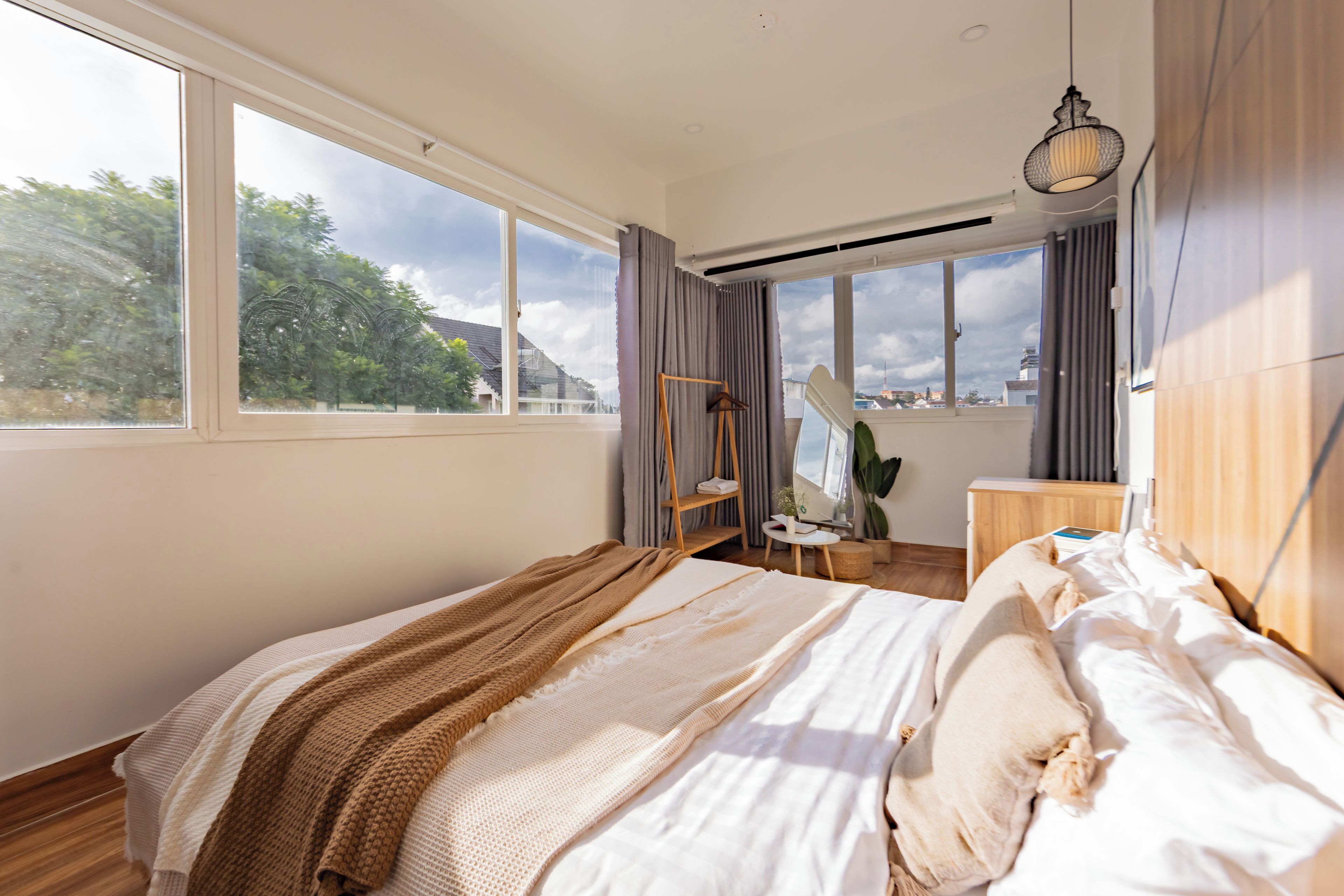 A bedroom with a large window, a bed with white bedding, a wooden headboard, and a hanging light fixture.