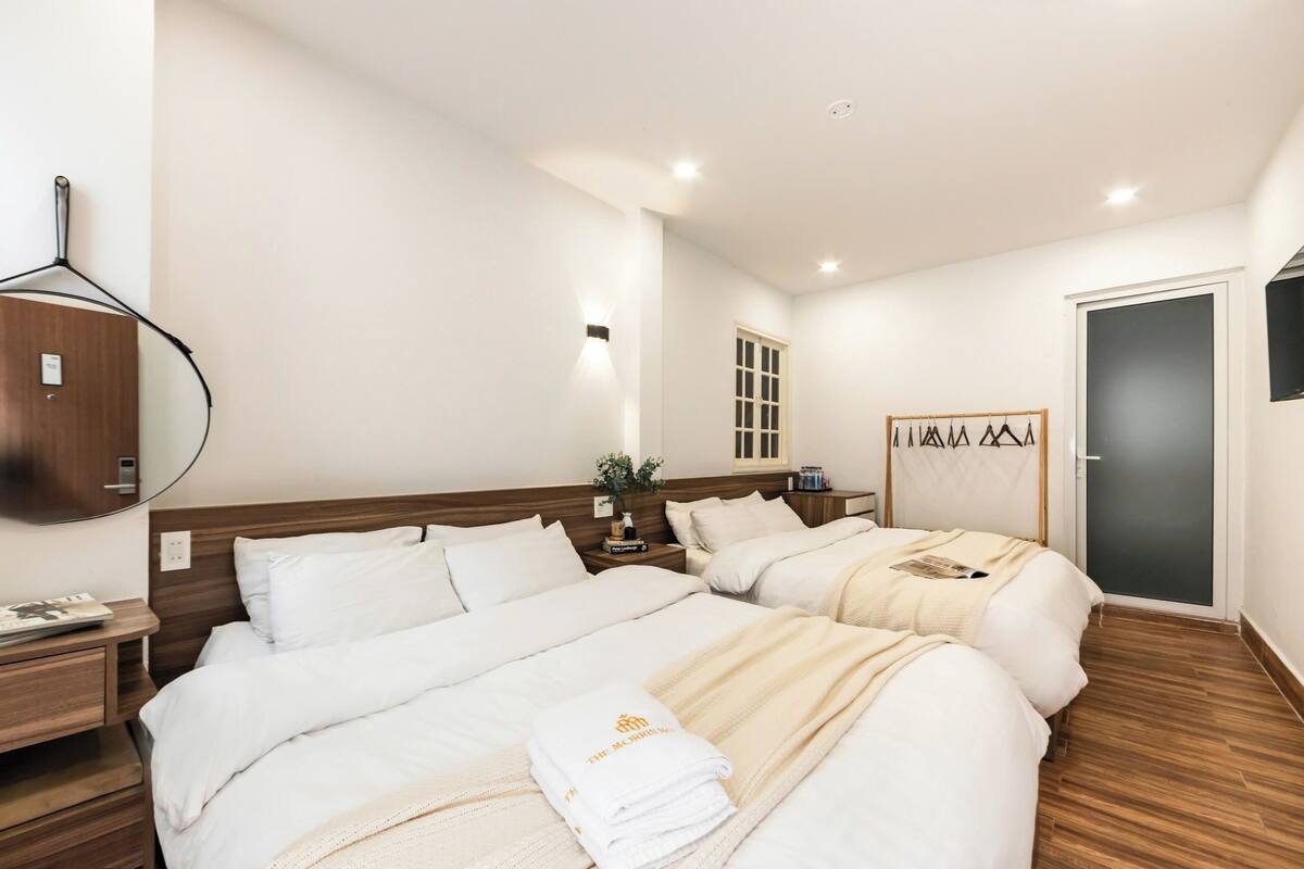 Une chambre d’hôtel avec deux lits, un plancher en bois, un grand miroir, une petite table avec une plante et une armoire.