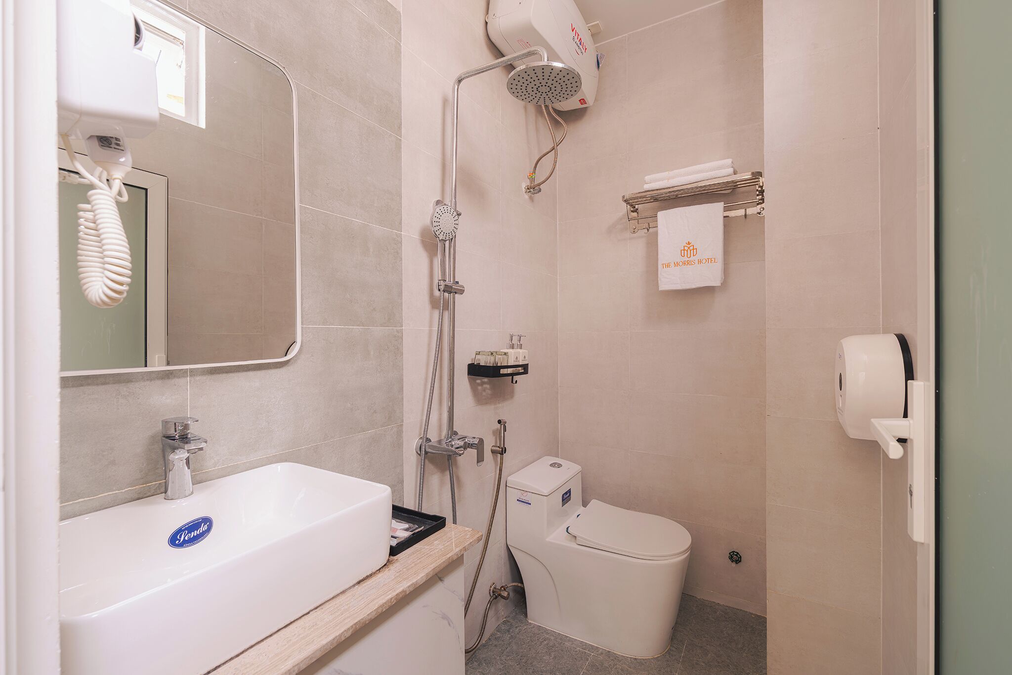 Une salle de bain avec un lavabo blanc, des toilettes, une douche avec un pommeau de douche amovible et un porte-serviettes avec une serviette.