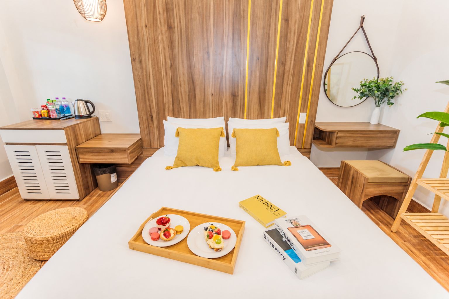 A hotel room with a bed, bedside tables, a small desk, a mirror, and a plant.
