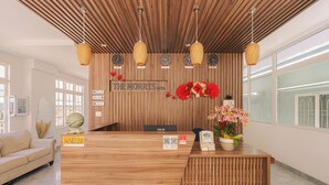 A hotel reception desk with a wooden finish, a reception area, and a wall-mounted clock. - The Morris Central Hotel - O'TEL (Xuan Huong - Da Lat)