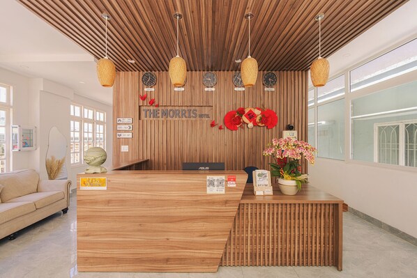 A hotel reception desk with a wooden finish, a reception area, and a wall-mounted clock. - The Morris Hotel - Central Dalat (Xuan Huong - Da Lat)