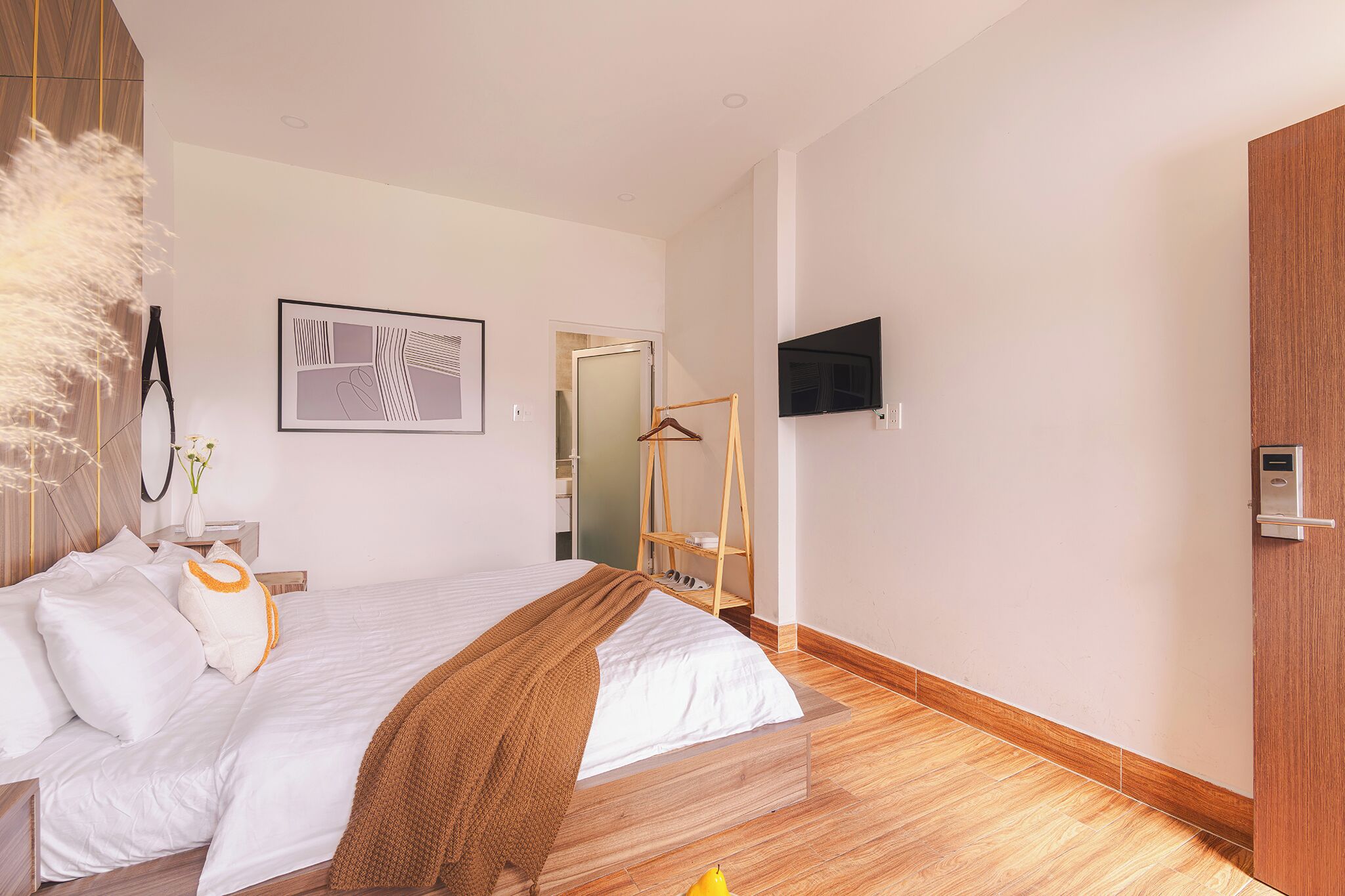 A modern hotel room with a large bed, a mounted TV, and a wooden wardrobe.