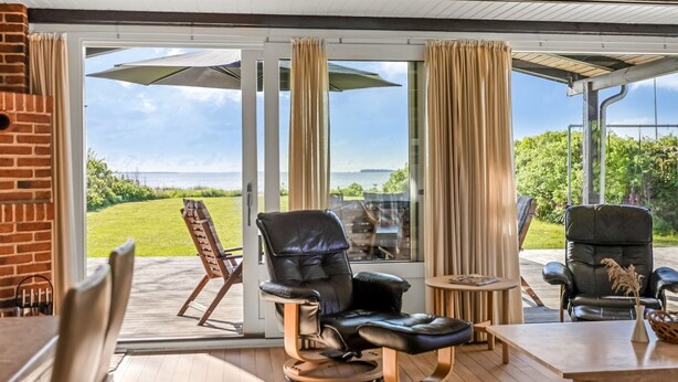 Un espace extérieur abrité, aménagé avec des fauteuils en cuir et une table en bois, et offrant une vue sur la mer.