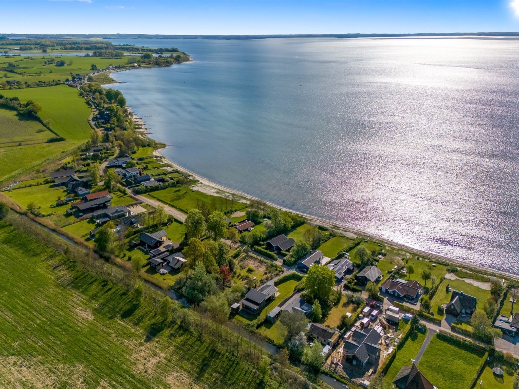 Luchtbeeld van een woongebied met huizen aan de waterkant, omringd door groene velden en een groot waterlichaam.
