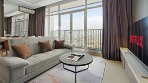 A modern living room with a grey sofa, a round coffee table, and a large TV screen displaying the Netflix logo. - Omira by Kozystay  - Cengkareng (Jakarta)