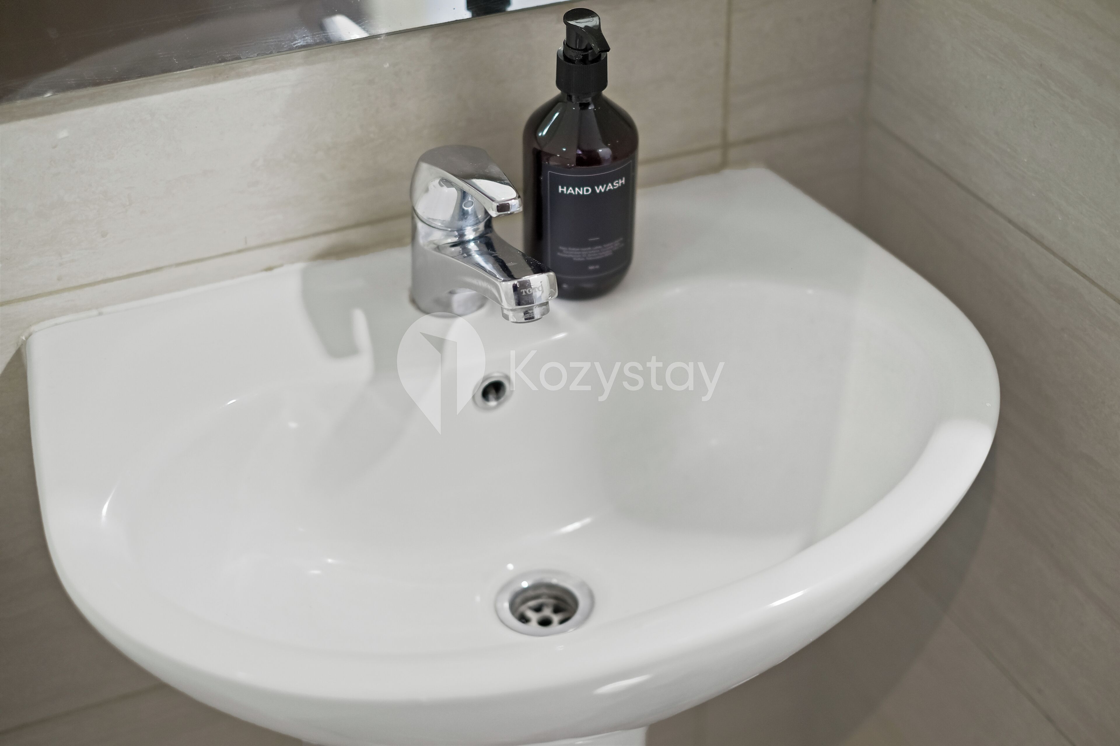 A white bathroom sink with a chrome faucet and a bottle of hand wash soap.
