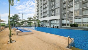 A modern building with a swimming pool, wooden deck, and lounge chairs. - Omira by Kozystay  - Cengkareng (Jakarta)