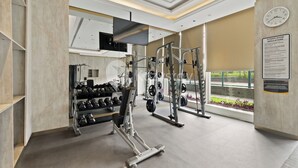 A modern gym with weightlifting equipment, dumbbells, and a wall-mounted clock. - Omira by Kozystay  - Cengkareng (Jakarta)