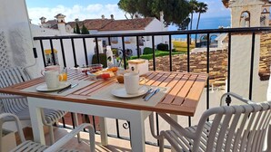 Ein Balkon mit einem Frühstückstisch, der auf eine Küstenlandschaft mit traditionellen Gebäuden und Meerblick blickt.