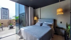 Et moderne soveværelse med en stor seng, en glasdør til en balkon og udsigt over byen.