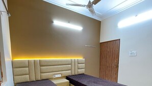 A bedroom with two beds, a ceiling fan, recessed lighting, and a wooden door. - Host varanasi (Varanasi)