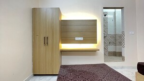 A room with a wooden wardrobe, a bench with a light underneath, and a patterned rug on the floor. - Host varanasi (Varanasi)
