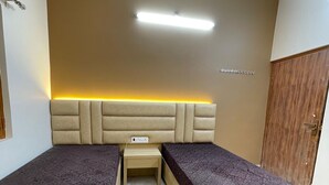 A bedroom with two single beds, a bedside table, a ceiling fan, and a wardrobe. - Host varanasi (Varanasi)