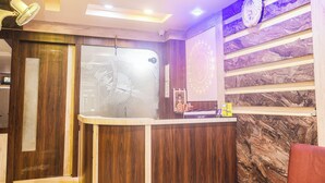 A reception area with a wooden reception desk, a clock, and a wall with a marble-like pattern. - Hotel Kasturi Continental (Bhopal)