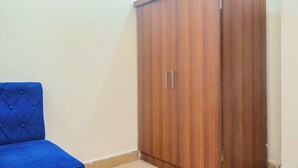 A room with a wooden wardrobe and a blue upholstered chair. - Hotel Kasturi Continental (Bhopal)