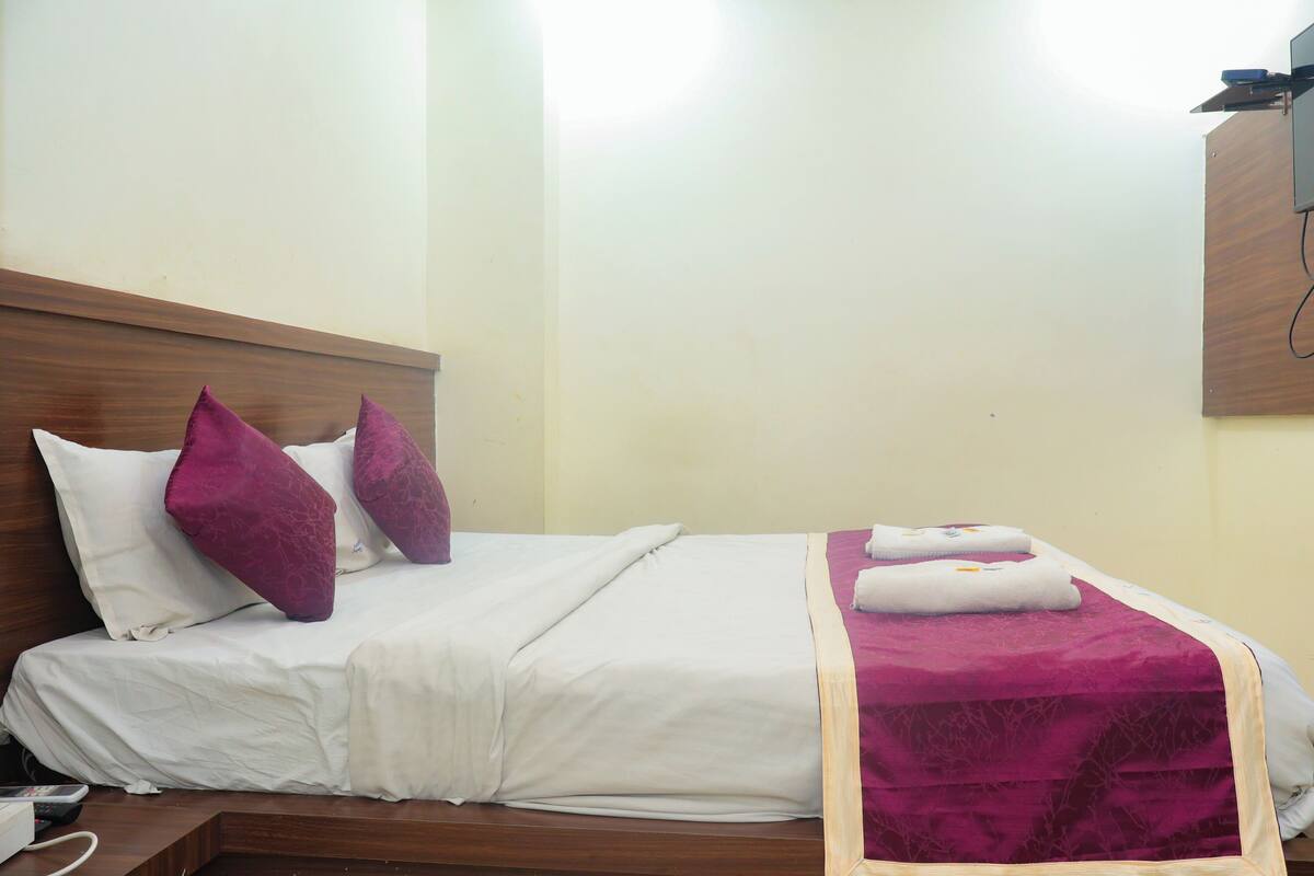 A neatly made bed with white linens and purple pillows, a wooden headboard, and a purple throw blanket.
