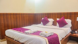 A double bed with white bedding and purple accents, a wooden headboard, and a bedside table with a phone and charger. - Hotel Kasturi Continental (Bhopal)