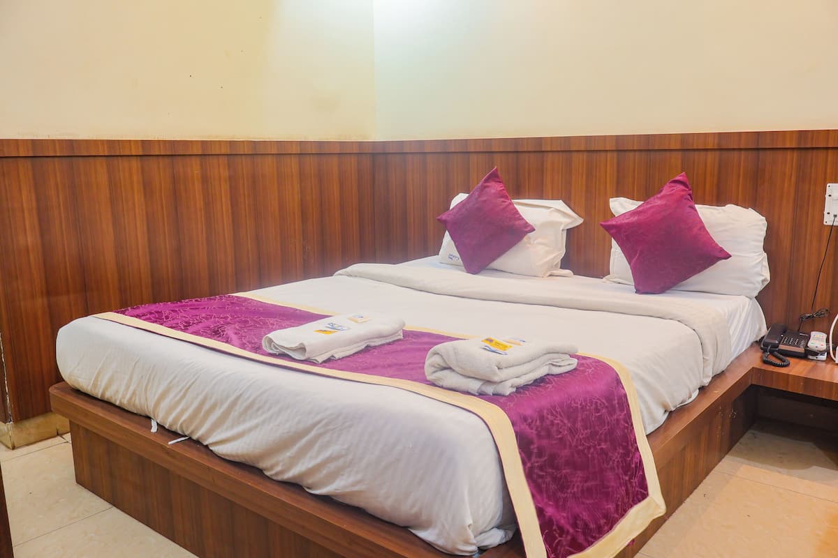 A double bed with white bedding and purple accents, a wooden headboard, and a bedside table with a phone and charger.