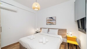 A modern bedroom with a large bed, a bedside table with a lamp, a wall-mounted artwork, and a window. - Erato Residential Complex-Two Bedroom Loft No Pool Access (Kavala)