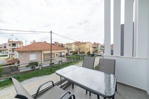 Un balcone con tavolo e sedie, affacciato su una zona residenziale con case e cielo sereno.