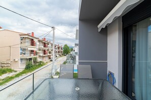 Un balcone con ringhiera in vetro, vista sui palazzi vicini e cielo sereno.