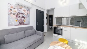 Et moderne opholdsrum med en grå sofa, en gul stol, et køkken med hvide skabe og et stort blomsterbillede på væggen.
