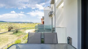 A modern balcony with a glass railing overlooking a grassy landscape and distant hills. - Olympiada-Two Bedroom Loft No Pool Access (Kavala)