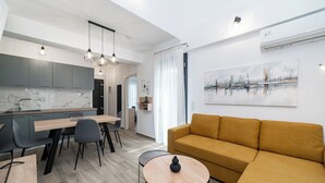 Una sala de estar moderna con sofá, una mesa de comedor con sillas, una zona de cocina y un cuadro abstracto grande en la pared.