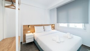 Una habitación de hotel moderna con cabecera de madera, ropa de cama blanca, una mesita de noche y un ventanal con vistas.