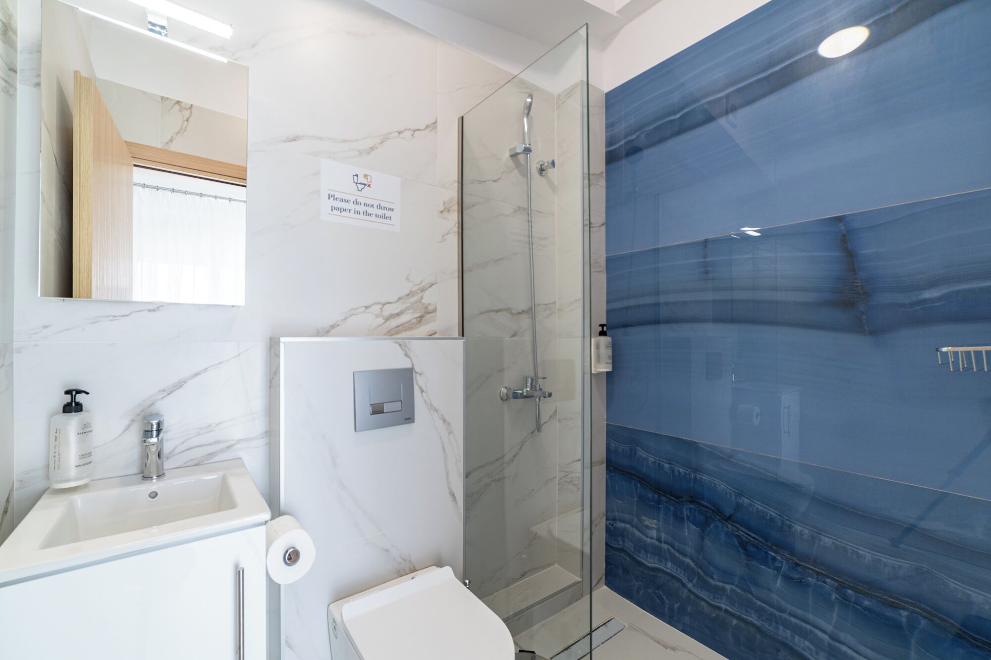 A bathroom with a marble vanity, a glass shower enclosure, and a blue tiled wall.