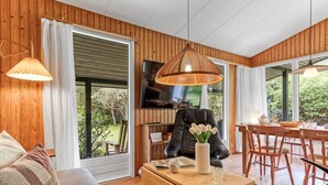 A cozy living room with wooden walls, a sofa, a coffee table, and a dining area with chairs and a table. - "Rikkart" - 400m from the sea by Interhome (Dannemare)