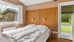 A bedroom with a wooden wall panel, a bed with white bedding, two bedside lamps, and a window with a view of the outdoors. - "Rikkart" - 400m from the sea by Interhome (Dannemare)
