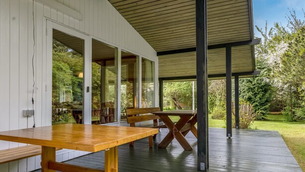 An outdoor wooden deck with a picnic table and benches, surrounded by glass doors leading to a lush garden. - "Rikkart" - 400m from the sea by Interhome (Dannemare)