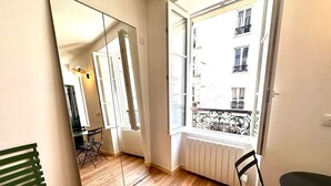 A room with a large mirror, a radiator, a window with a view of buildings, and a table with chairs. - Sunny Paris flat heart of 11ème (Paris)