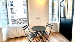 A small room with a round table and four chairs, a radiator, a window with a view of buildings, and a door. - Sunny Paris flat heart of 11ème (Paris)