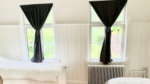 Een kamer met twee bedden, witte wanden, houten vloer en zwarte gordijnen voor de ramen.